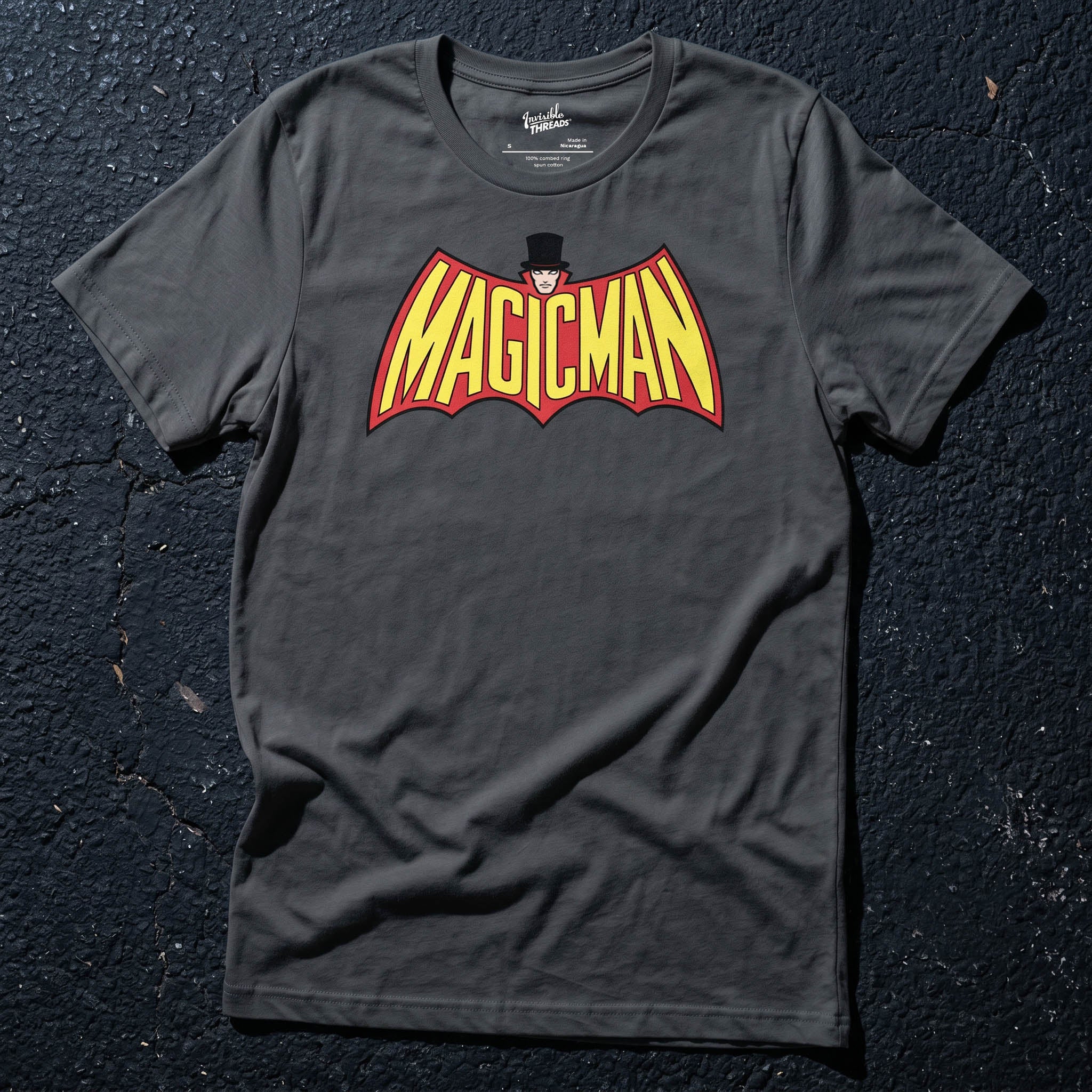 Asphalt gray Magicman t-shirt featuring bold yellow and red superhero-inspired lettering with a top-hatted magician