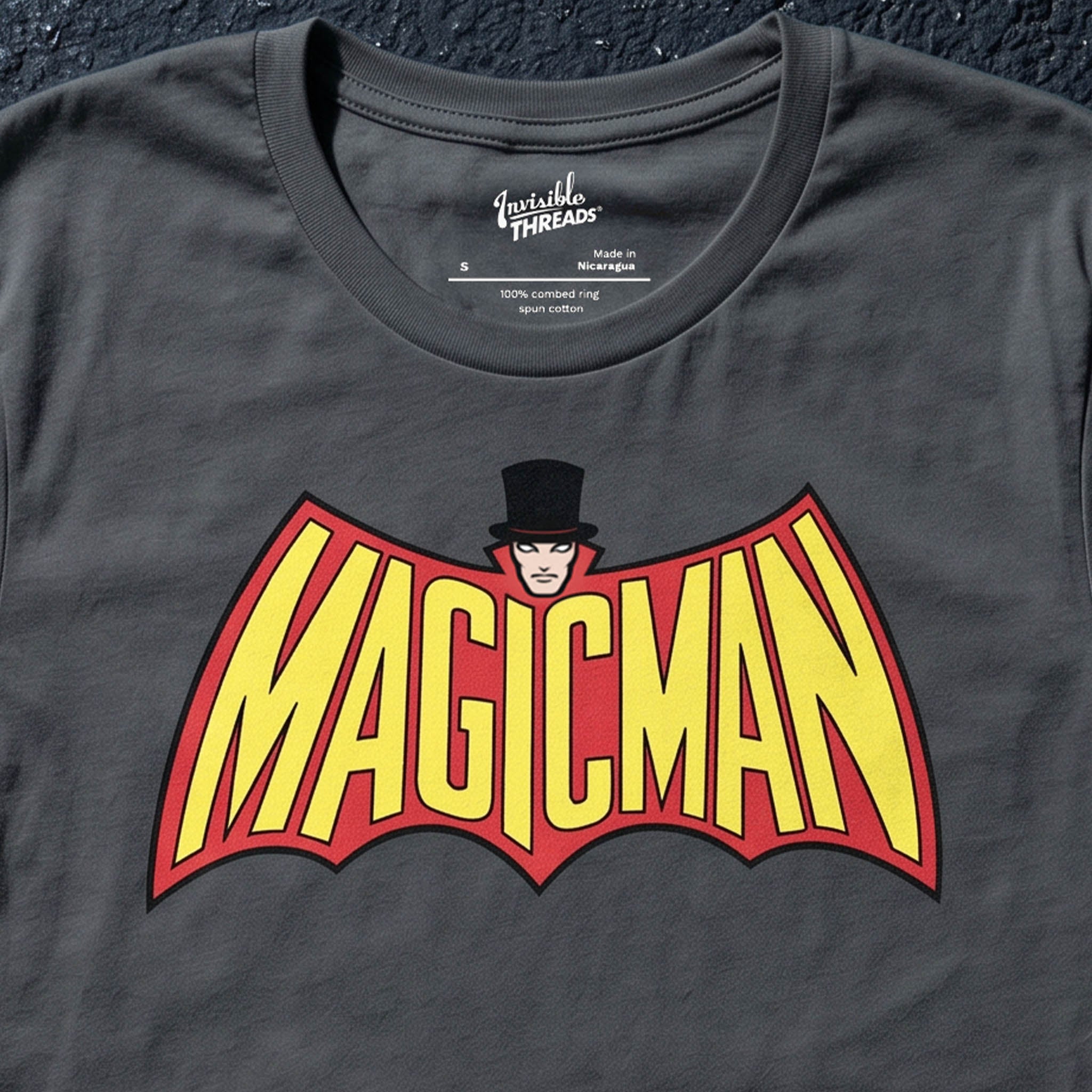 Asphalt gray Magicman t-shirt featuring bold yellow and red superhero-inspired lettering with a top-hatted magician